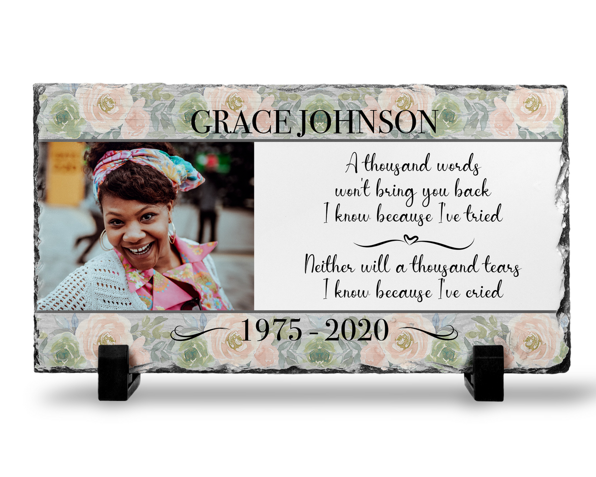 Floral memorial photo slate with a woman’s portrait, sample name and dates, and A Thousand Words tribute on black stands